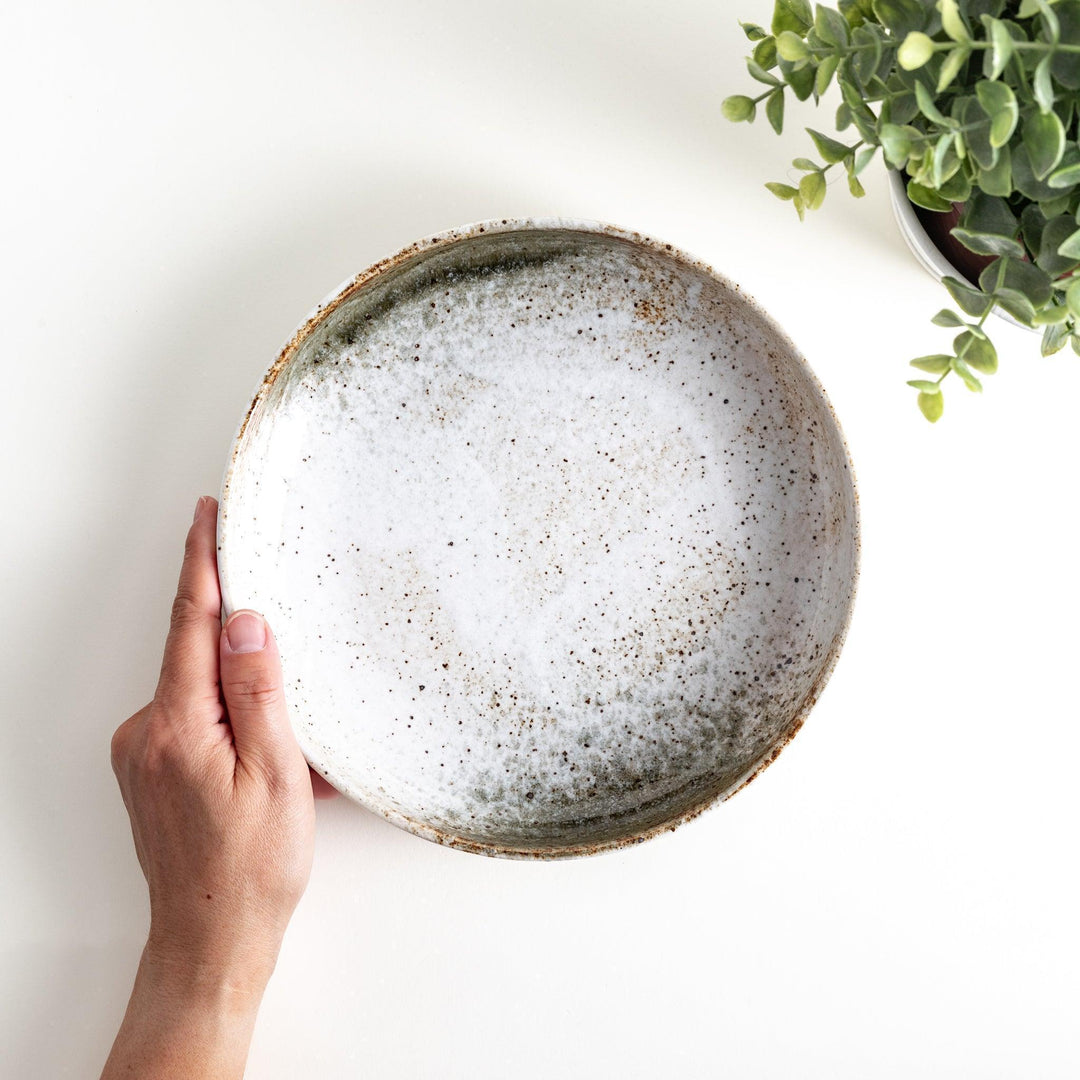 A pasta bowl with a speckled cream and brown glaze, displaying an earthy, organic design.