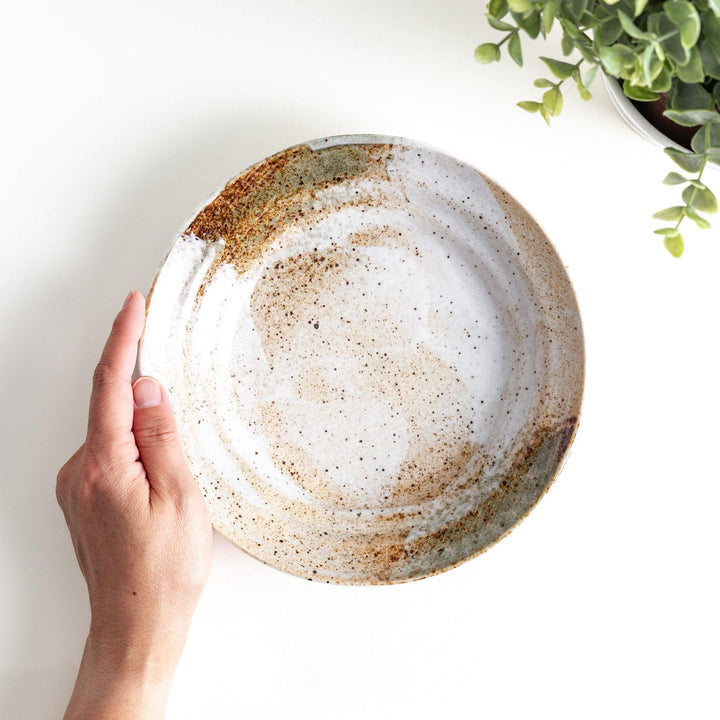 A salad plate with a speckled cream and brown glaze, featuring an earthy, organic design.