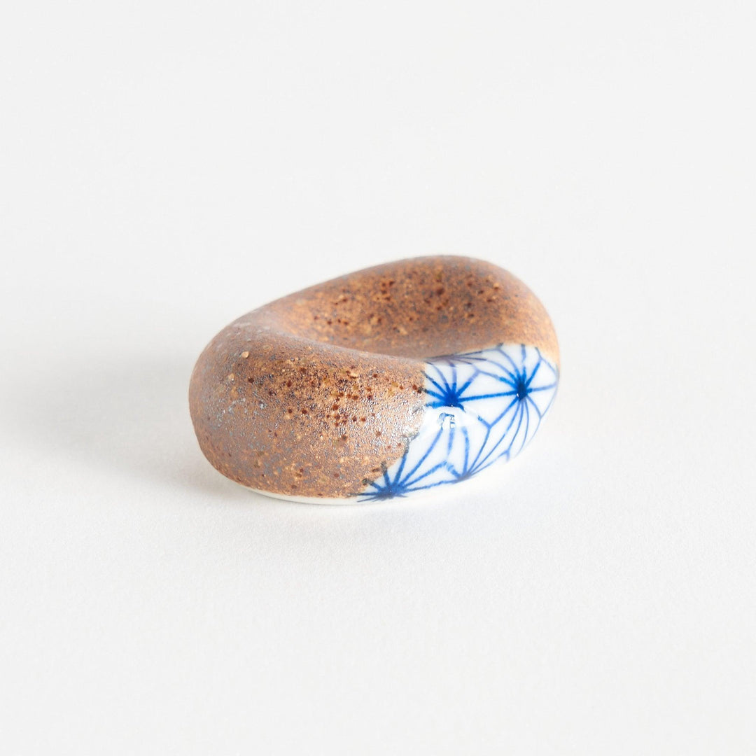 A brown and white rounded ceramic chopstick rest with a partial geometric pattern.