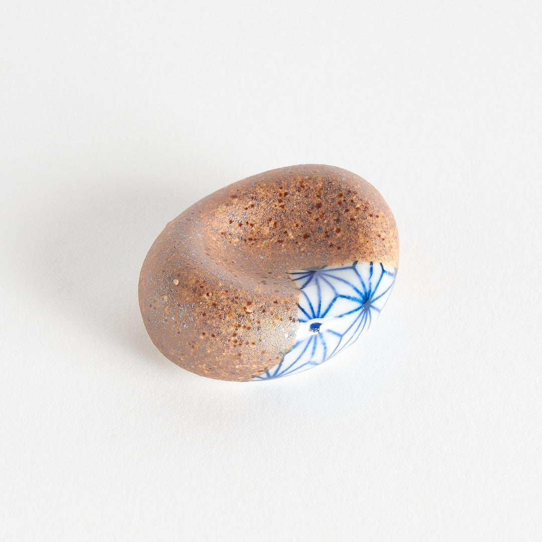 A brown and white rounded ceramic chopstick rest with a partial geometric pattern.