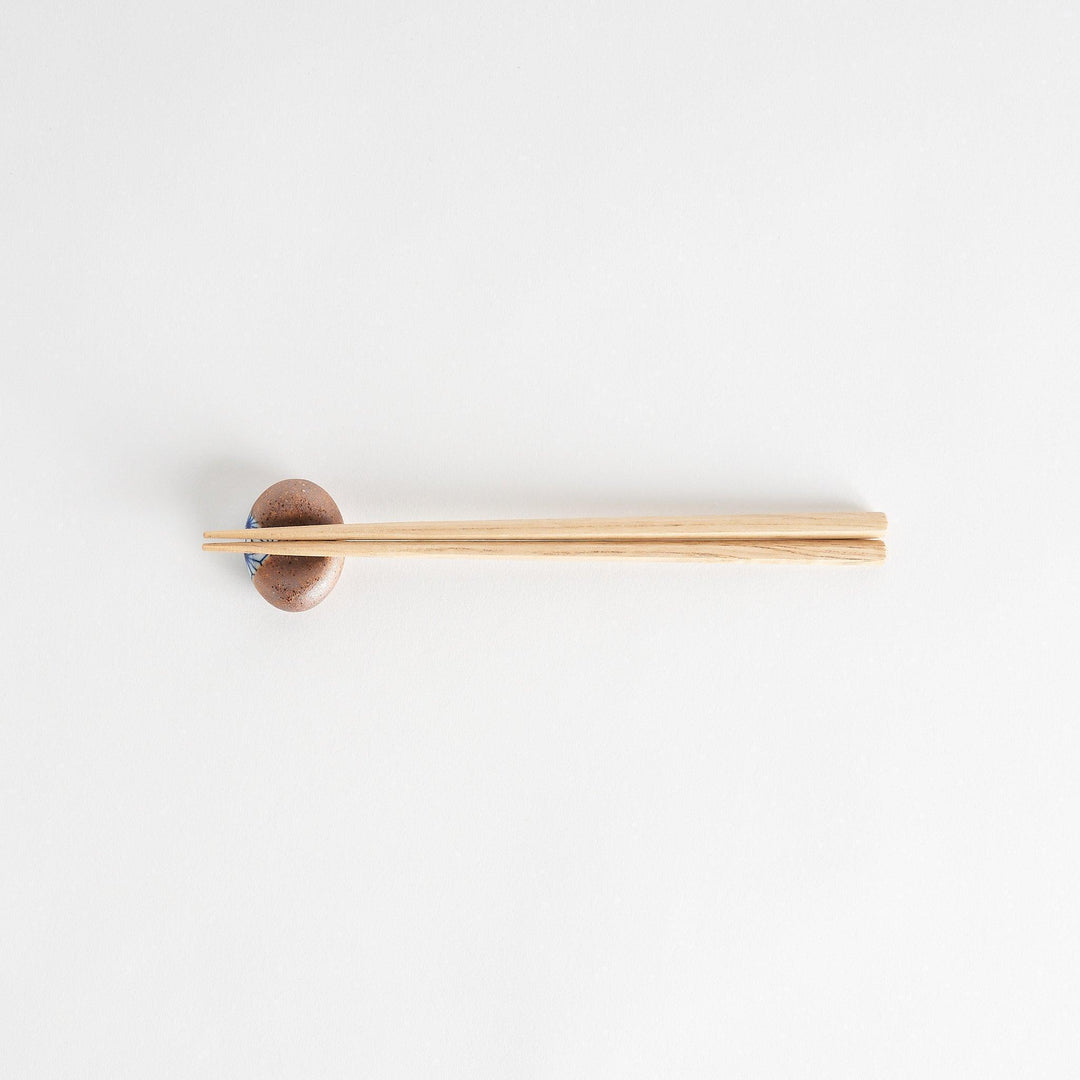 A brown and white rounded ceramic chopstick rest with a partial geometric pattern.