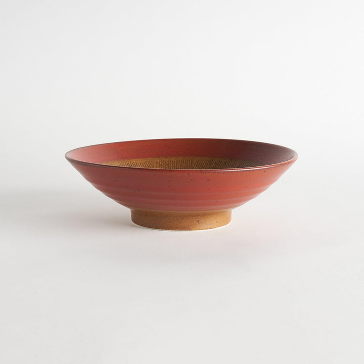 A shallow bowl featuring a red outer rim and a golden-brown interior with a fine radial pattern.