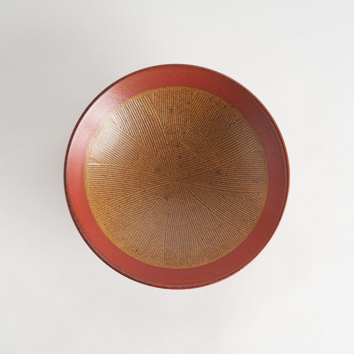 A shallow bowl featuring a red outer rim and a golden-brown interior with a fine radial pattern.