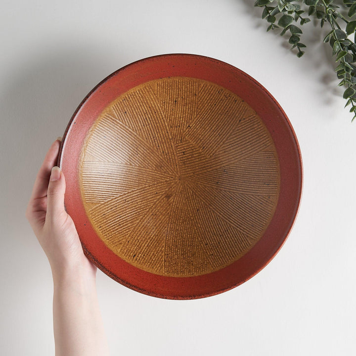 A shallow bowl featuring a red outer rim and a golden-brown interior with a fine radial pattern.