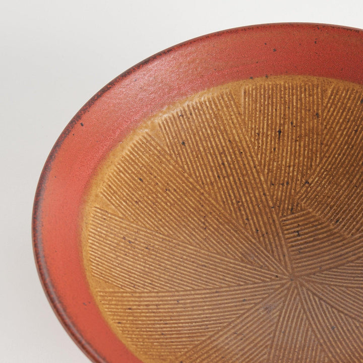 A shallow bowl featuring a red outer rim and a golden-brown interior with a fine radial pattern.