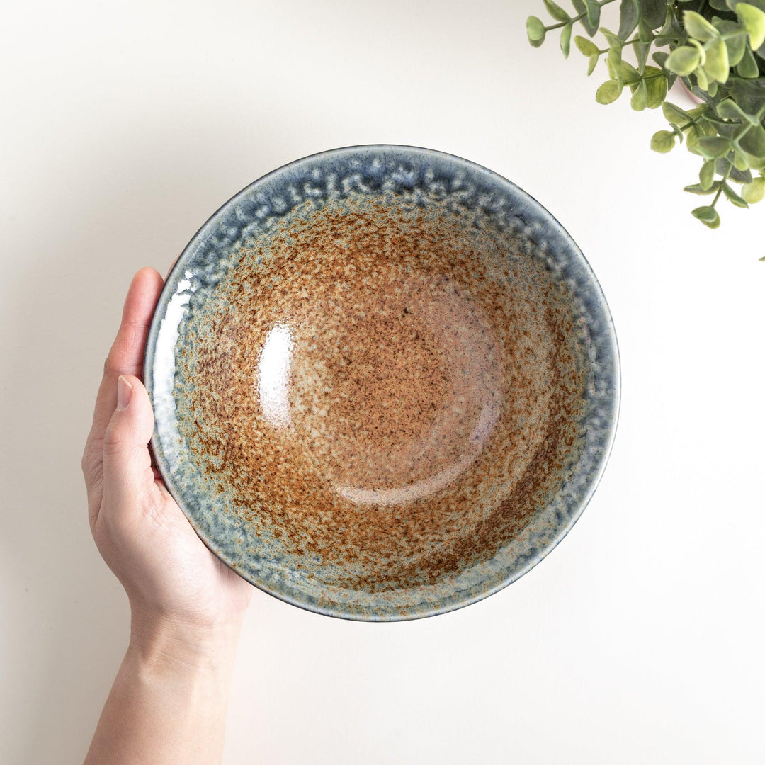 A deep ceramic bowl with a speckled glaze in shades of blue and brown, creating a textured, earthy appearance.