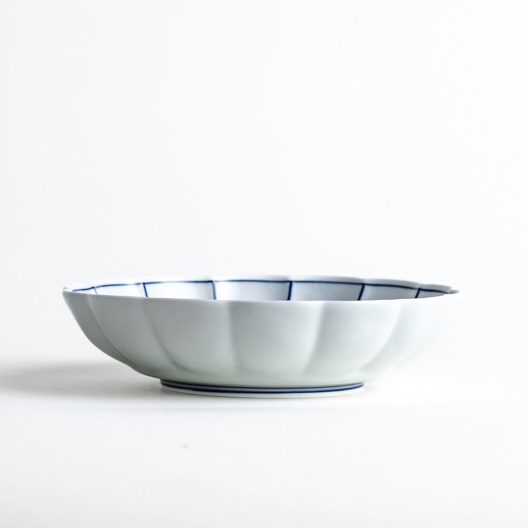 White cereal bowl with scalloped edges, featuring thin blue and red lines forming a petal-like design.