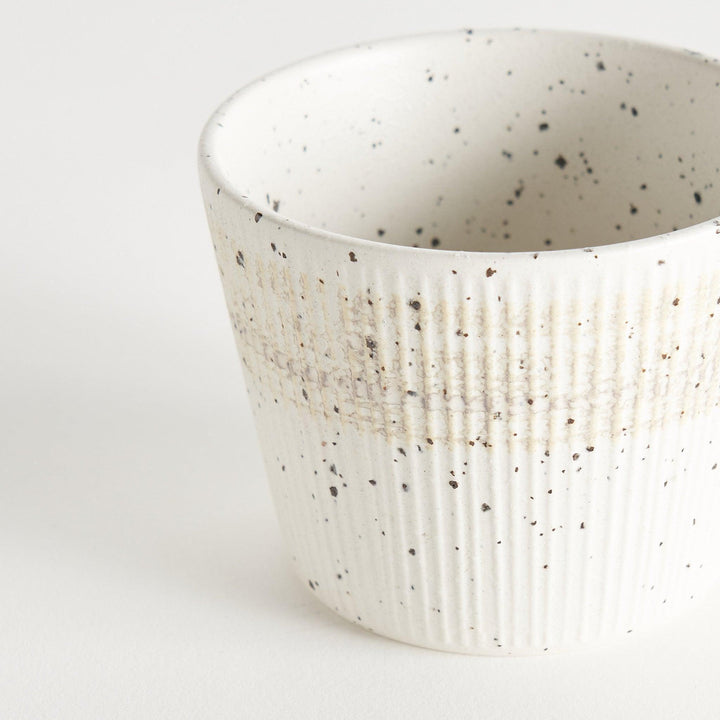 A small, off-white ceramic cup with a ribbed texture and subtle speckled design.