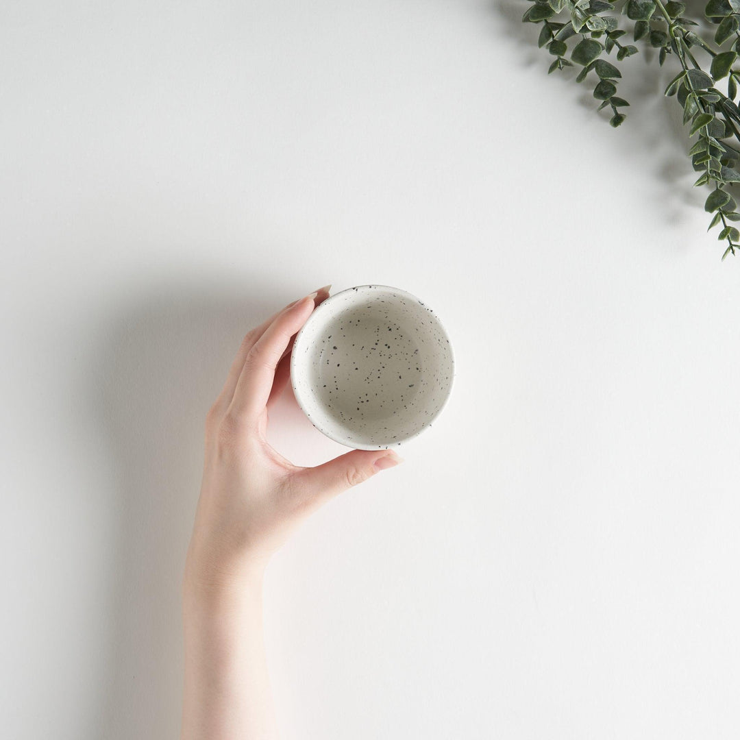 A small, off-white ceramic cup with a ribbed texture and subtle speckled design.