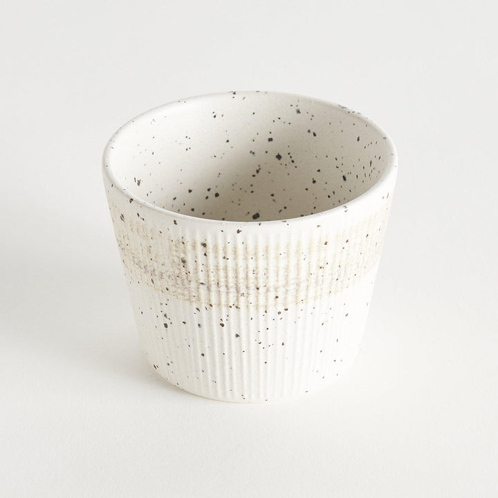 A small, off-white ceramic cup with a ribbed texture and subtle speckled design.