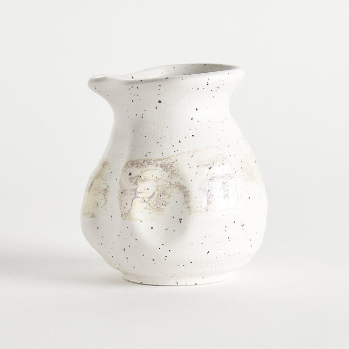 A small, off-white sauce pourer with a rounded shape, speckled glaze, and a slightly flared spout.