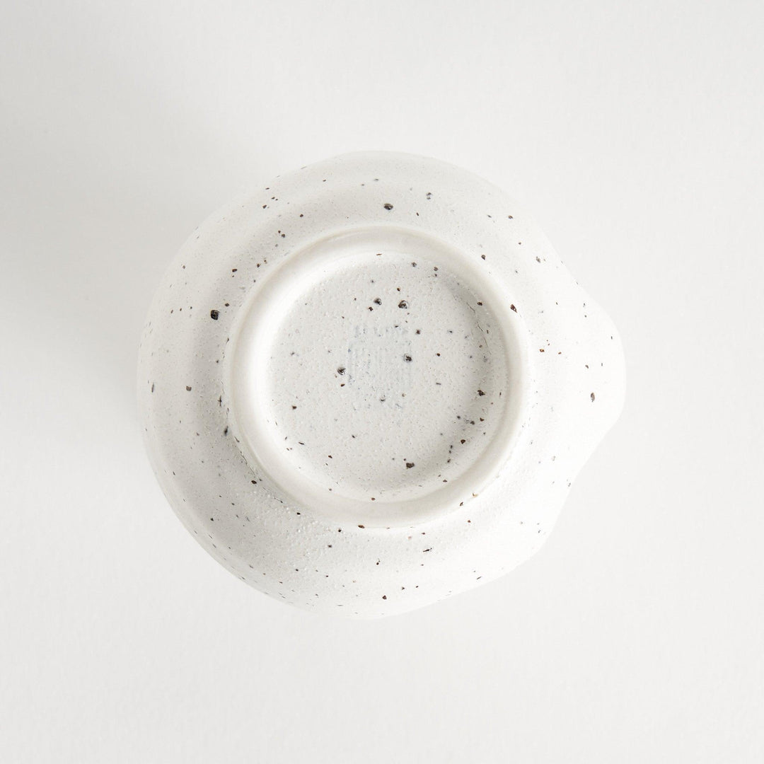 A small, off-white sauce pourer with a rounded shape, speckled glaze, and a slightly flared spout.