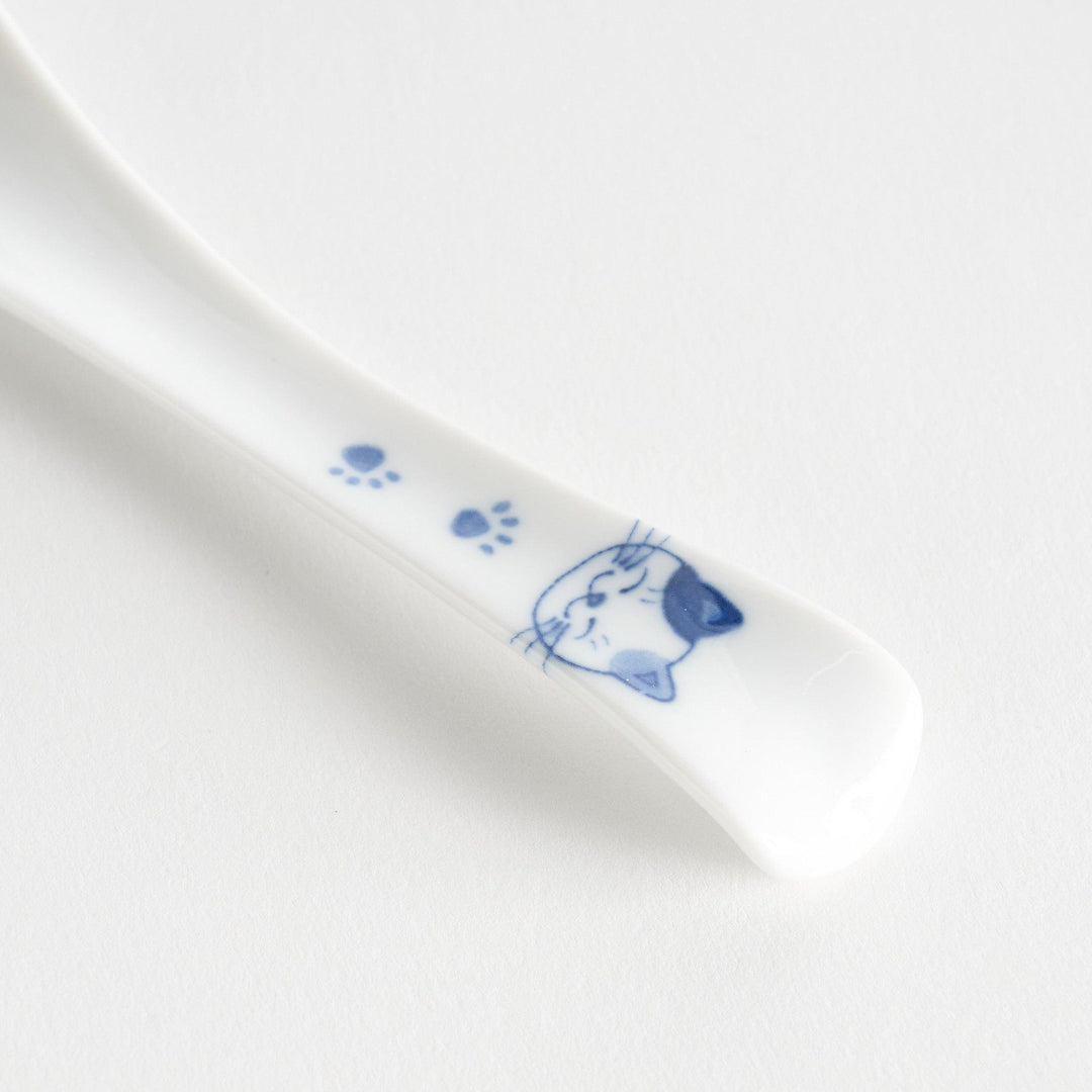 A white porcelain spoon with a blue cat face and paw prints on the handle.