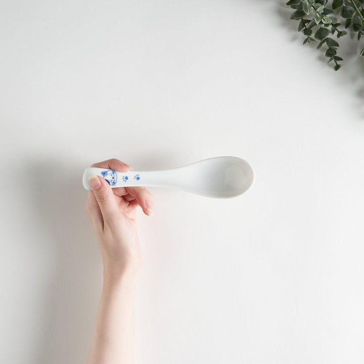 A white porcelain spoon with a blue cat face and paw prints on the handle.