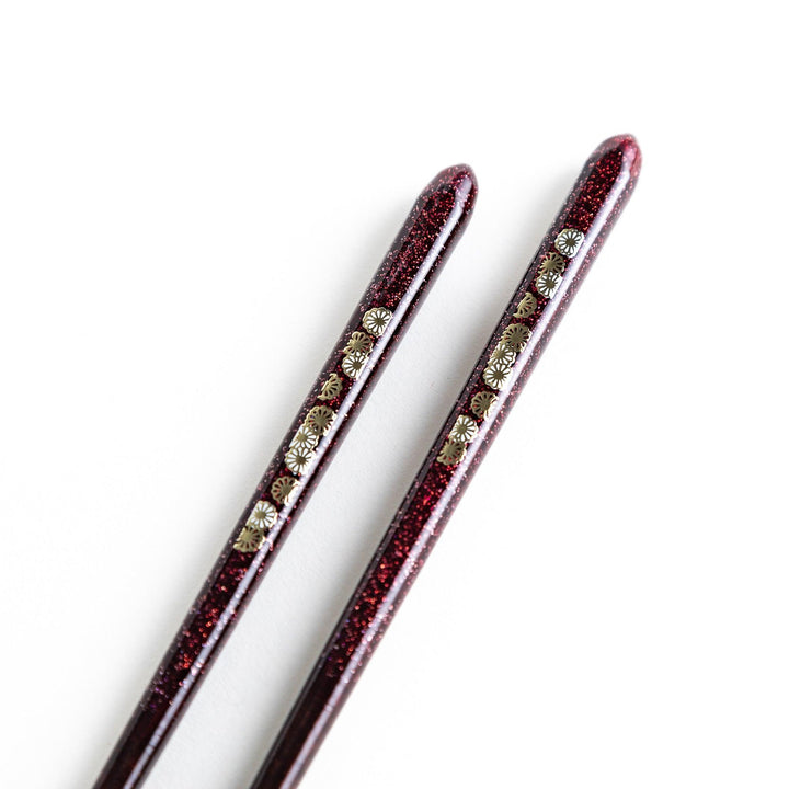 Two pairs of chopsticks, one in deep purple and the other in red, each decorated with subtle gold accents and a speckled finish.