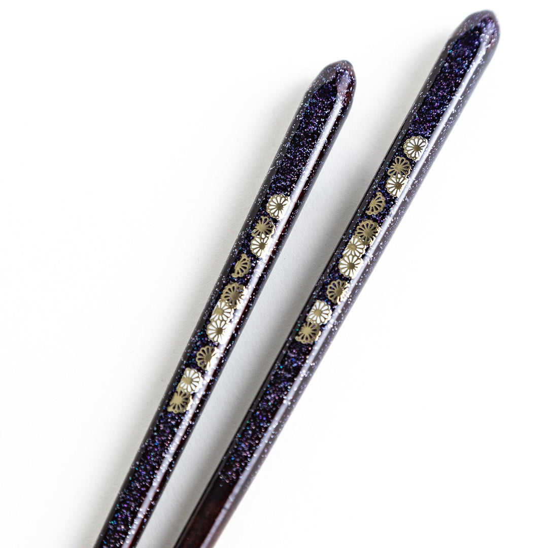 Two pairs of chopsticks, one in deep purple and the other in red, each decorated with subtle gold accents and a speckled finish.