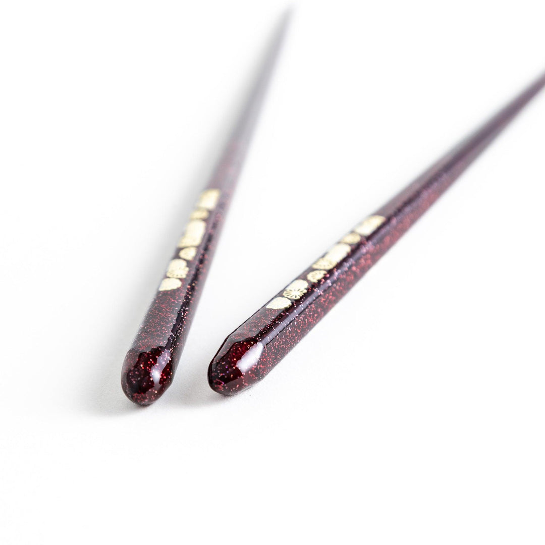 Two pairs of chopsticks, one in deep purple and the other in red, each decorated with subtle gold accents and a speckled finish.