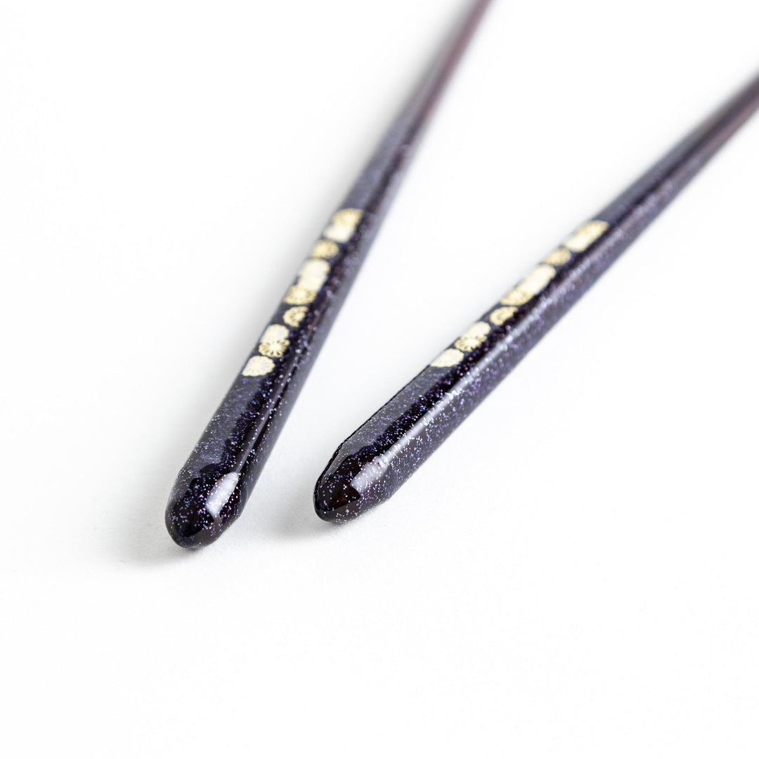 Two pairs of chopsticks, one in deep purple and the other in red, each decorated with subtle gold accents and a speckled finish.