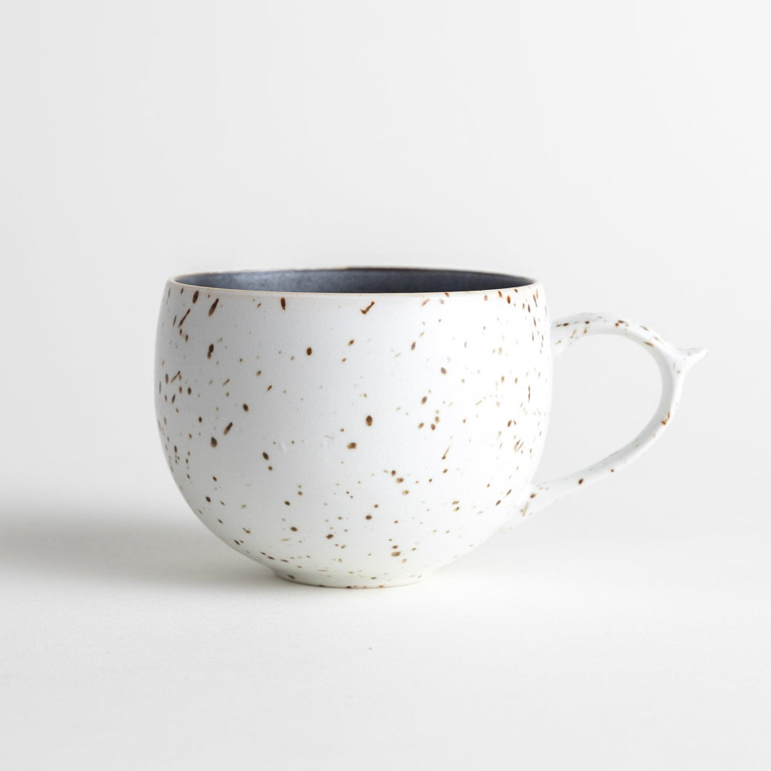 Ceramic mugs, one in matte black and the other in speckled white, with delicate curved handles.