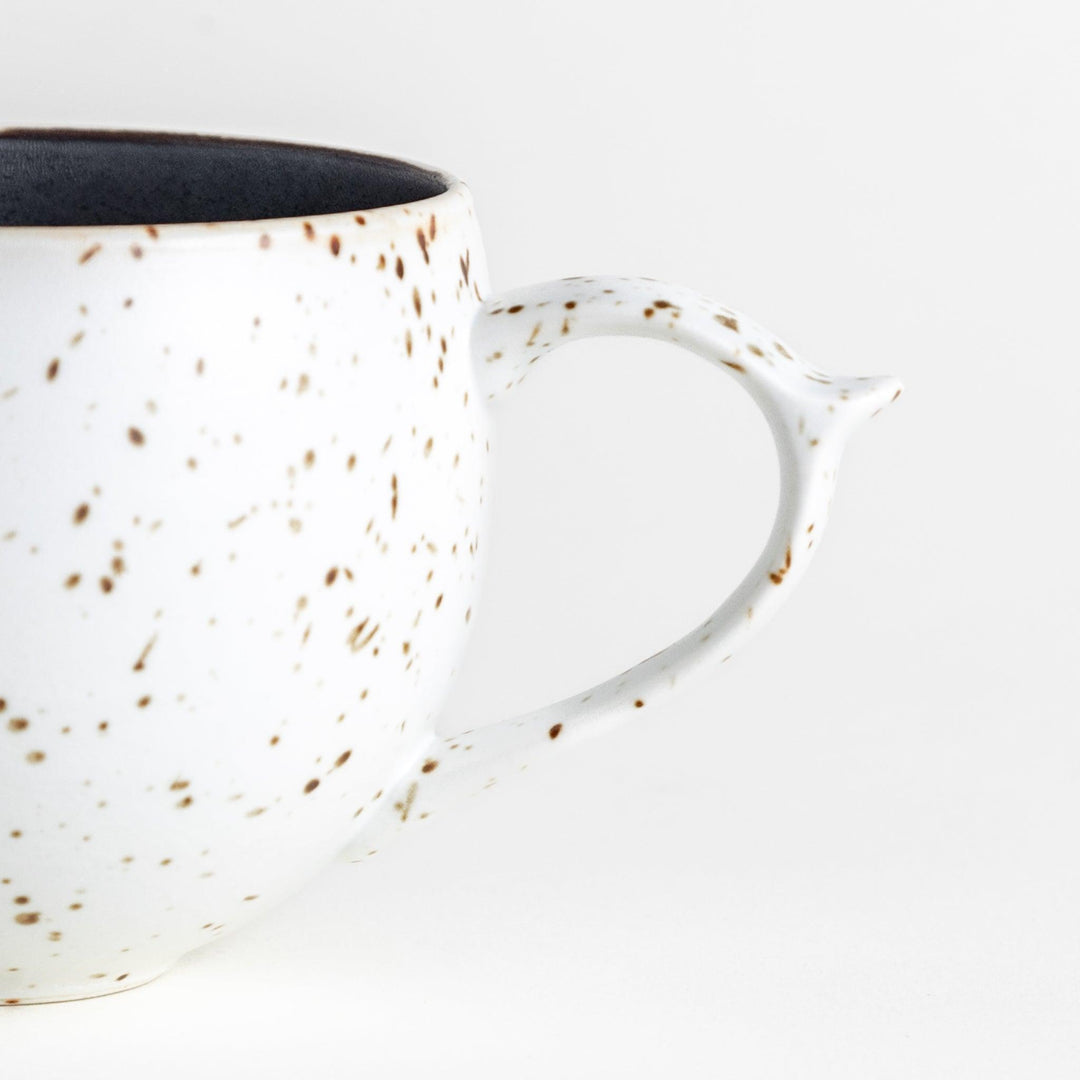 Ceramic mugs, one in matte black and the other in speckled white, with delicate curved handles.