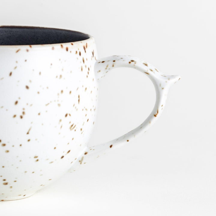 Ceramic mugs, one in matte black and the other in speckled white, with delicate curved handles.