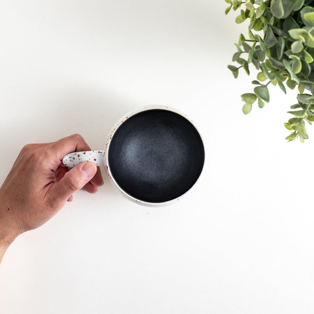 Ceramic mugs, one in matte black and the other in speckled white, with delicate curved handles.