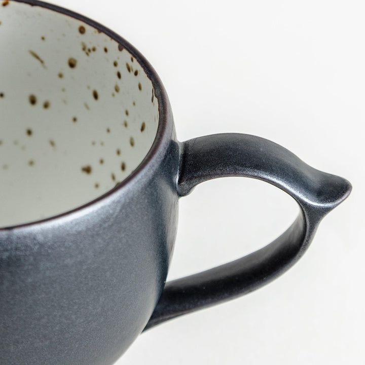 Ceramic mugs, one in matte black and the other in speckled white, with delicate curved handles.