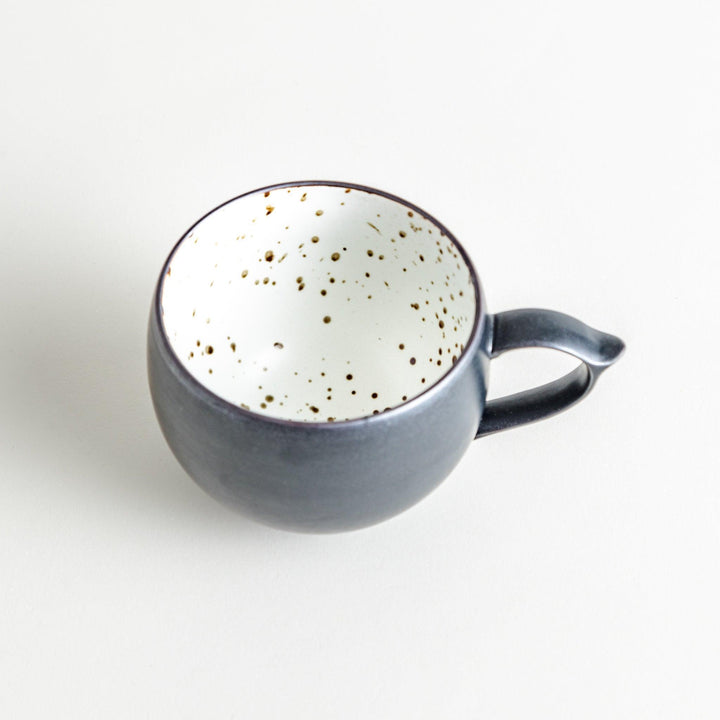 Ceramic mugs, one in matte black and the other in speckled white, with delicate curved handles.