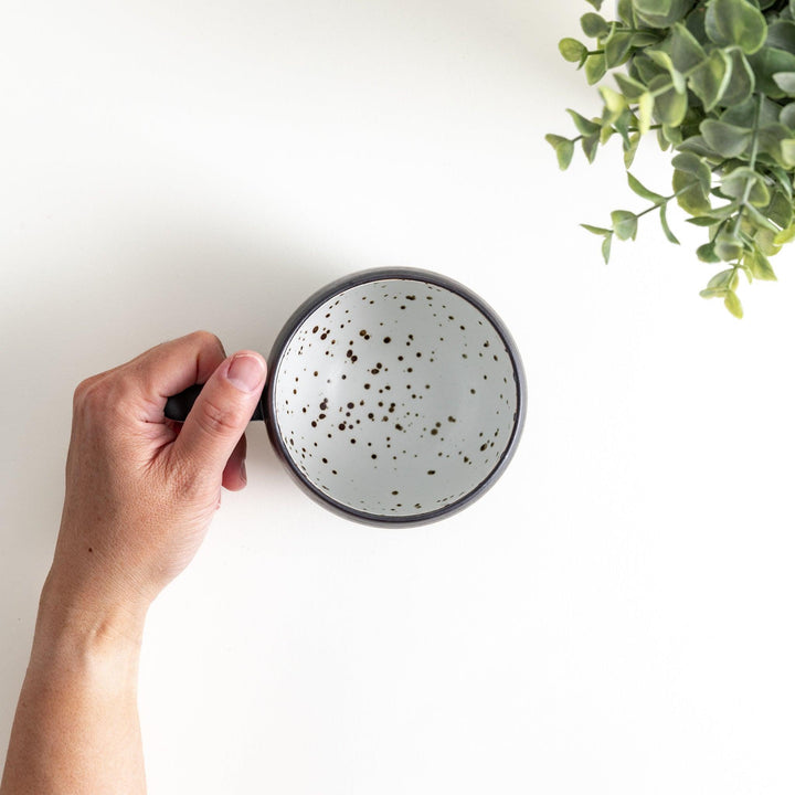 Ceramic mugs, one in matte black and the other in speckled white, with delicate curved handles.