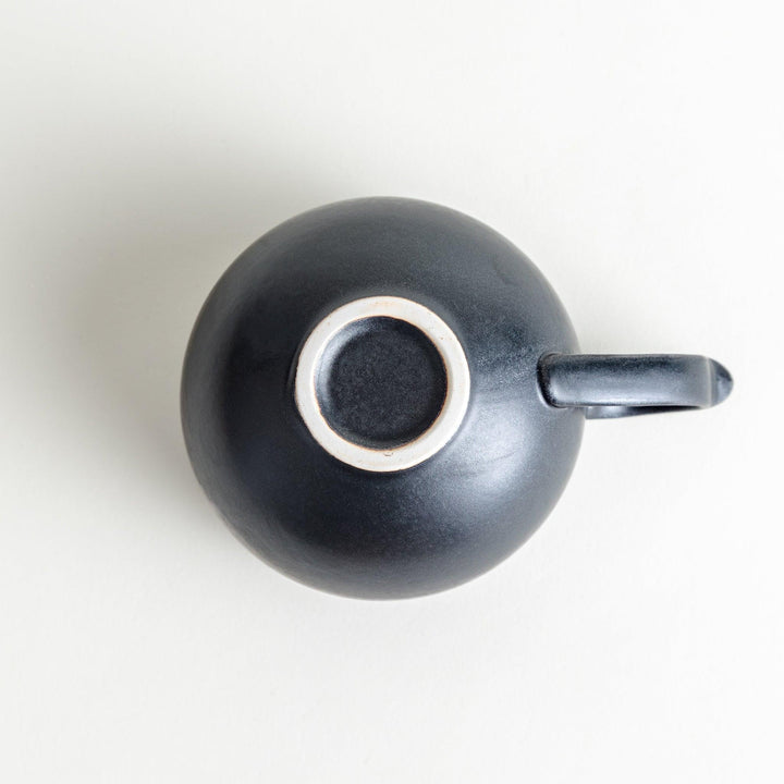 Ceramic mugs, one in matte black and the other in speckled white, with delicate curved handles.