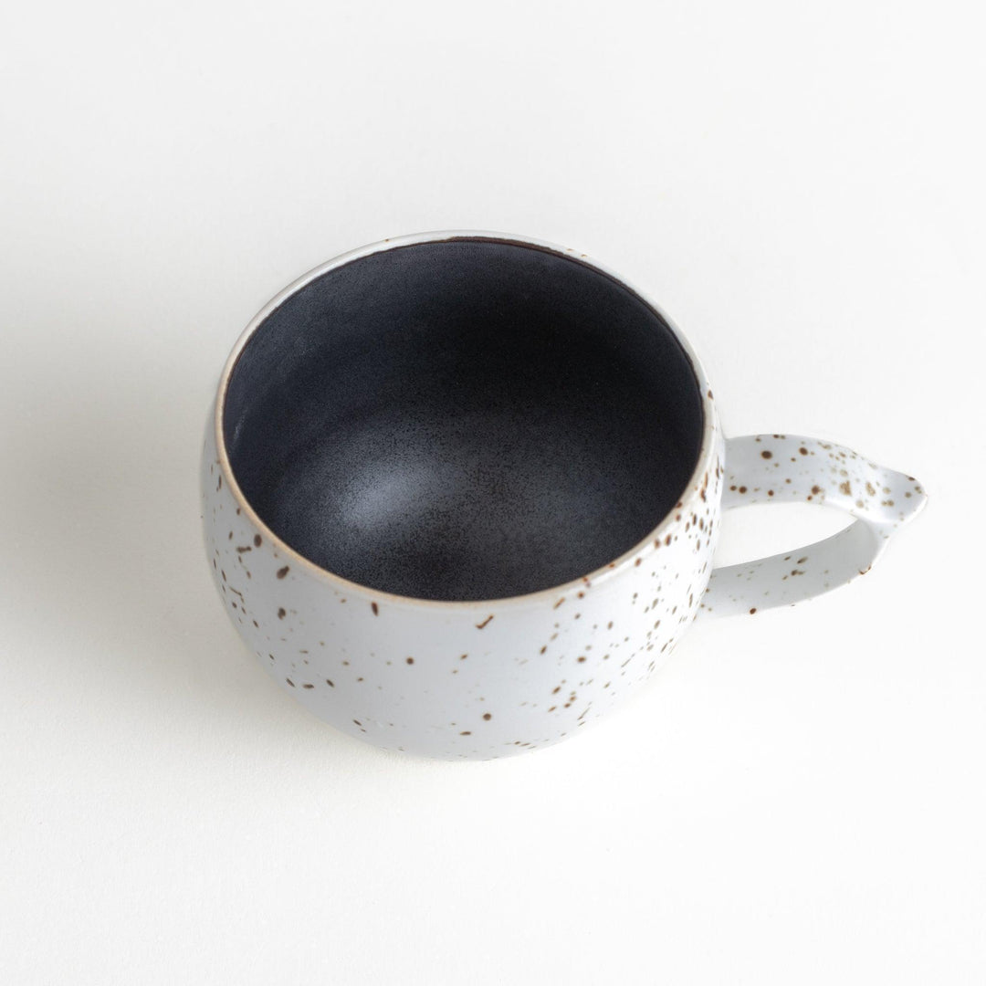 Ceramic mugs, one in matte black and the other in speckled white, with delicate curved handles.