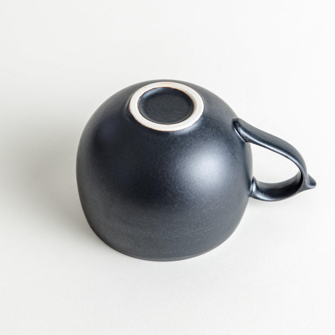 Ceramic mugs, one in matte black and the other in speckled white, with delicate curved handles.