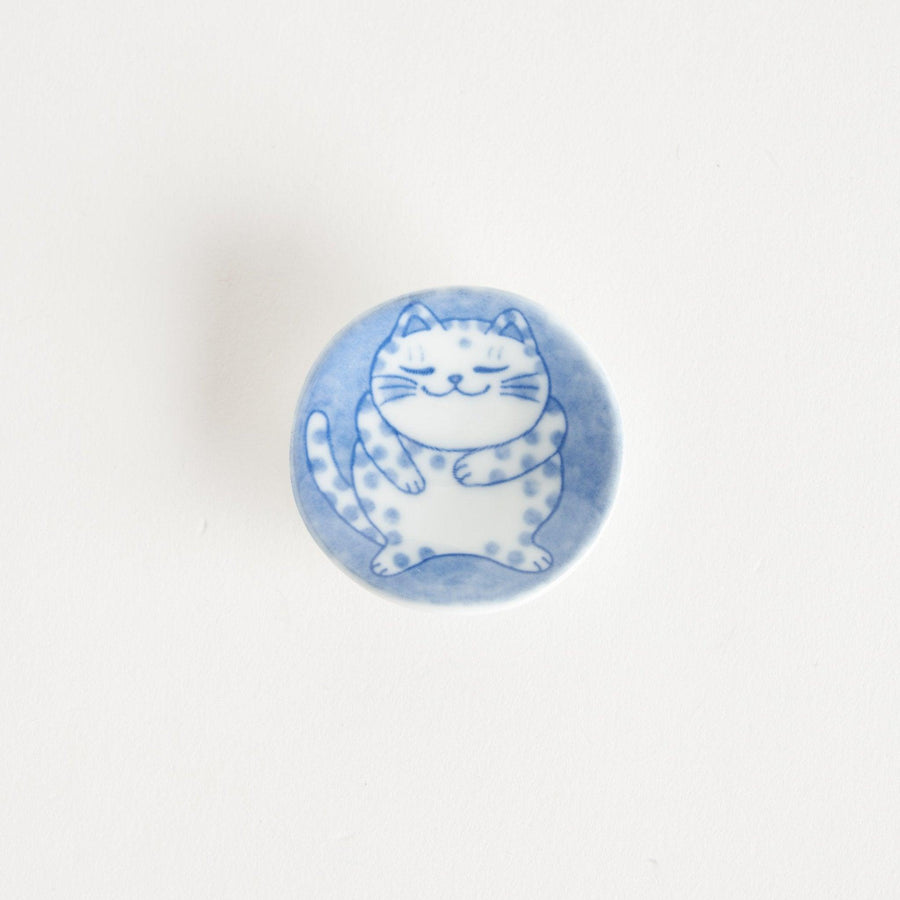 A round ceramic chopstick rest with a smiling, spotted cat illustration in blue.