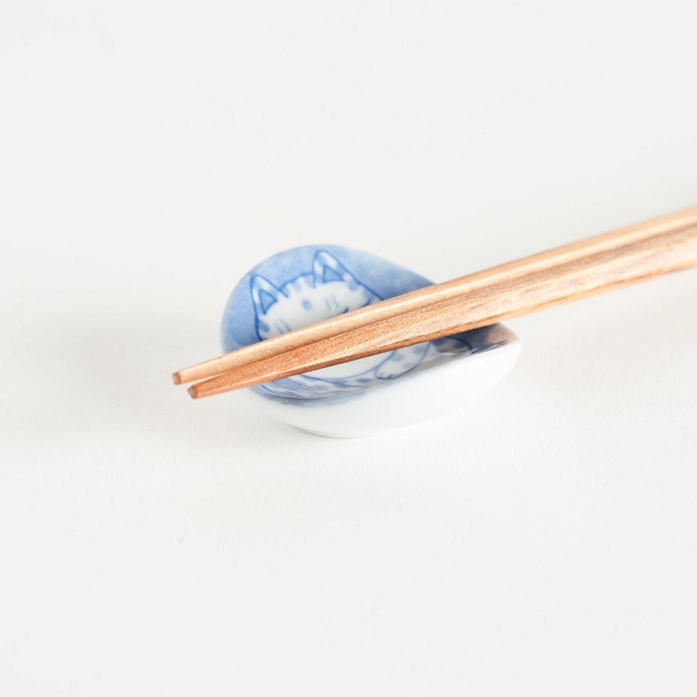 A round ceramic chopstick rest with a smiling, spotted cat illustration in blue.