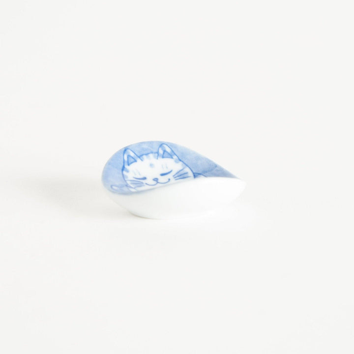 A round ceramic chopstick rest with a smiling, spotted cat illustration in blue.