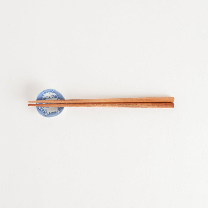 A round ceramic chopstick rest with a smiling, spotted cat illustration in blue.