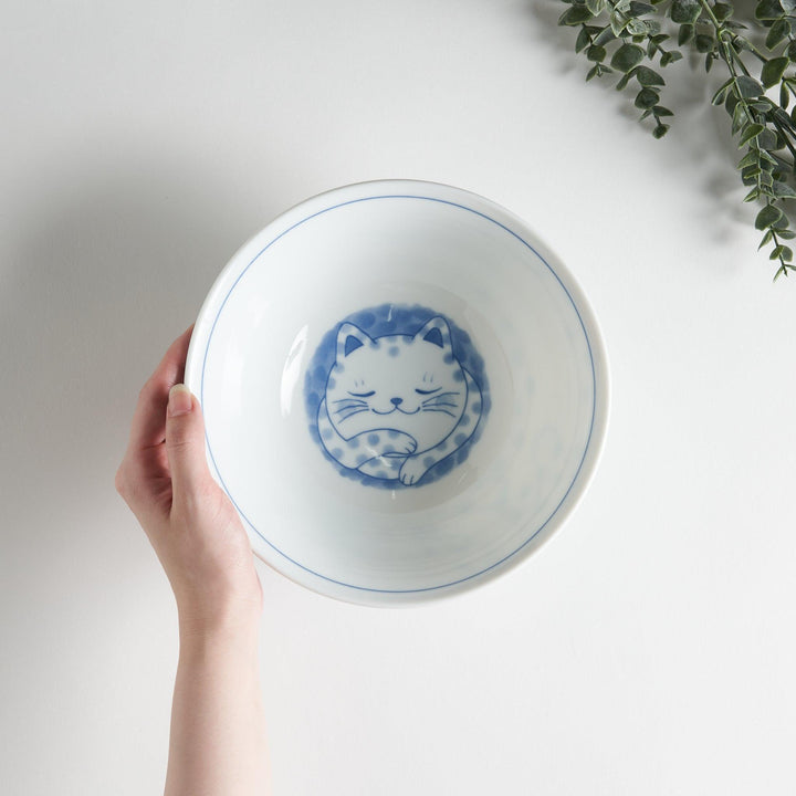 A ramen bowl with a design of a blue and white spotted cat, appearing cozy and content.