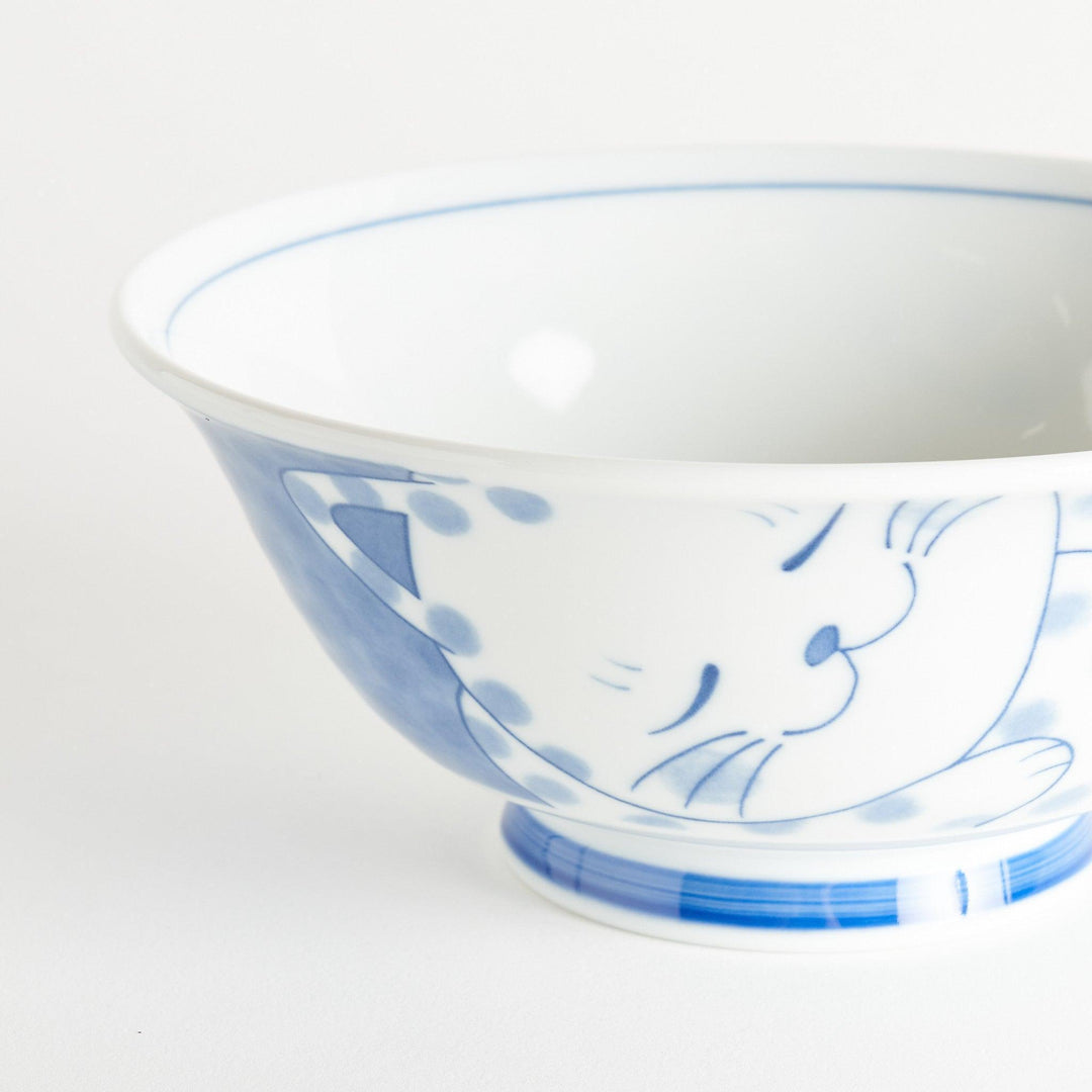 A ramen bowl with a design of a blue and white spotted cat, appearing cozy and content.