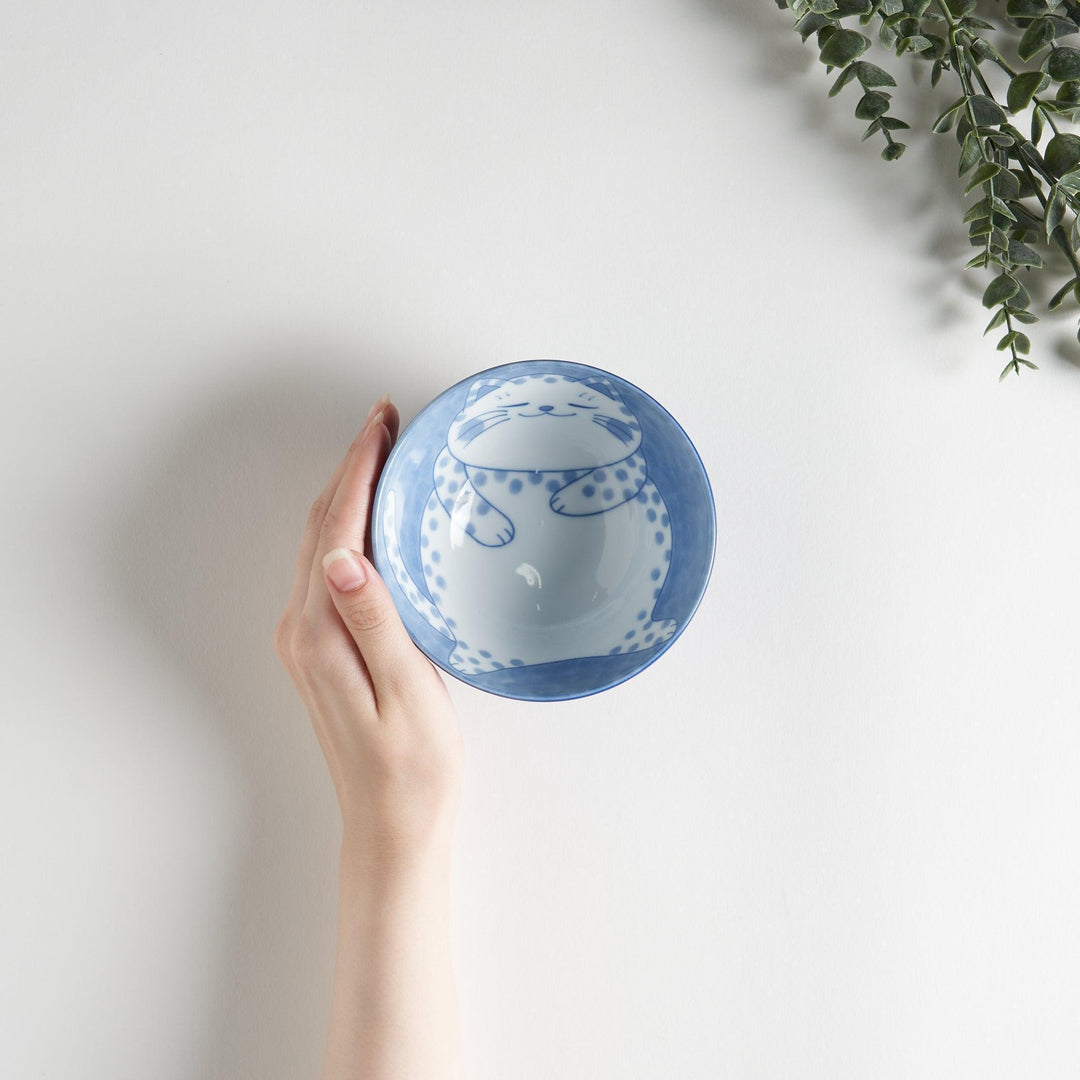 A rice bowl featuring a chubby blue-spotted white cat, sitting contentedly.