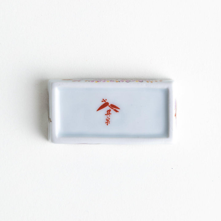 A ceramic chopstick rest shaped like a rectangular block, decorated with traditional Japanese patterns in blue, red, and green.