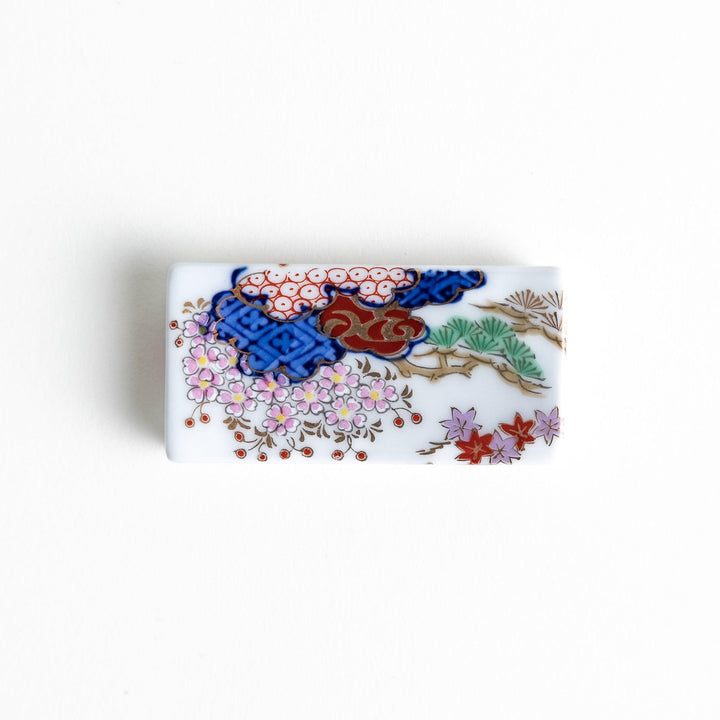 A ceramic chopstick rest shaped like a rectangular block, decorated with traditional Japanese patterns in blue, red, and green.