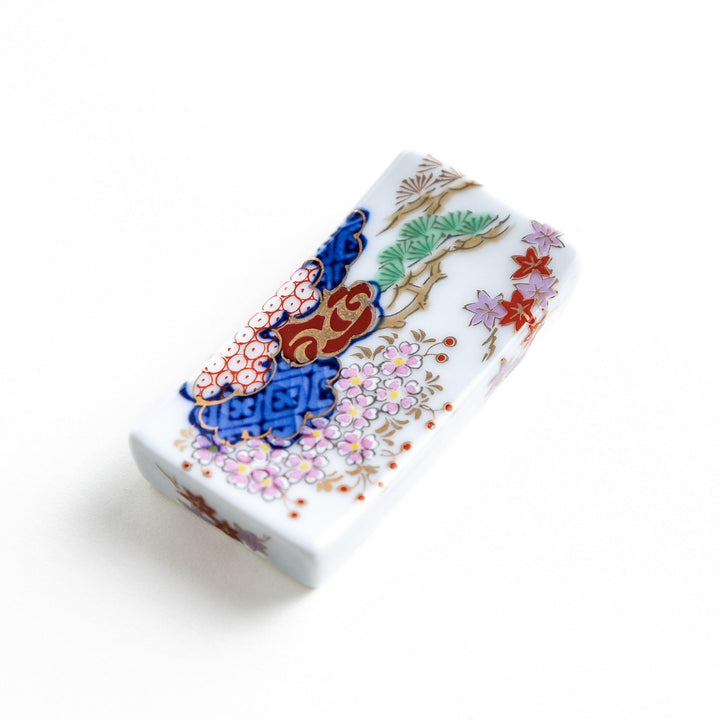 A ceramic chopstick rest shaped like a rectangular block, decorated with traditional Japanese patterns in blue, red, and green.