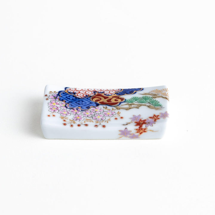 A ceramic chopstick rest shaped like a rectangular block, decorated with traditional Japanese patterns in blue, red, and green.