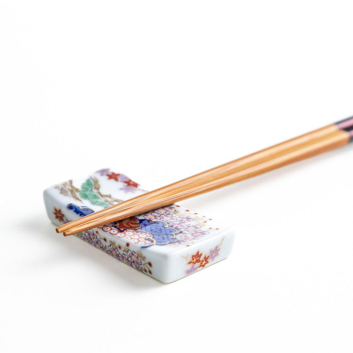 A ceramic chopstick rest shaped like a rectangular block, decorated with traditional Japanese patterns in blue, red, and green.