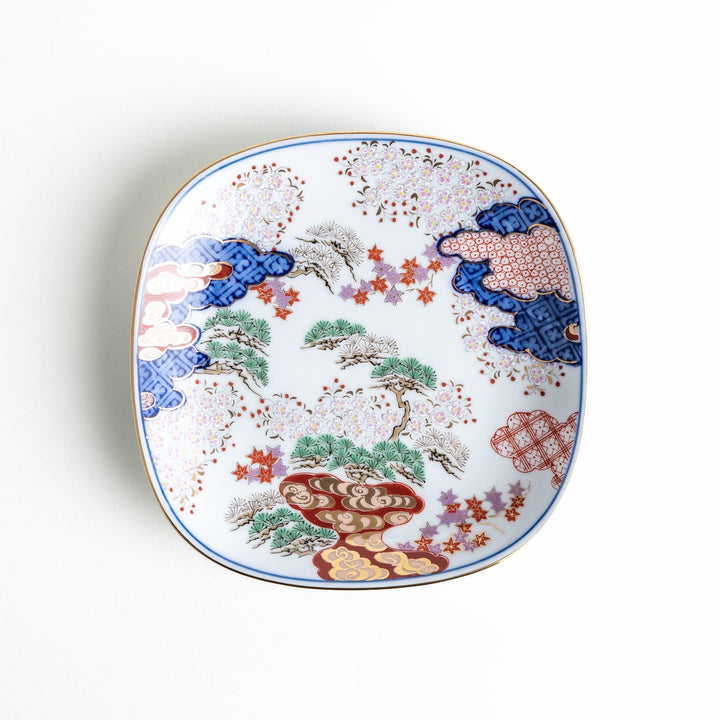 A square dessert plate featuring an intricate Japanese landscape with trees and clouds, surrounded by red and blue patterns on the border.