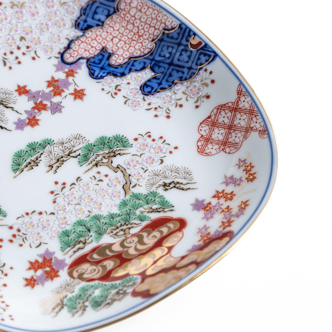 A square dessert plate featuring an intricate Japanese landscape with trees and clouds, surrounded by red and blue patterns on the border.