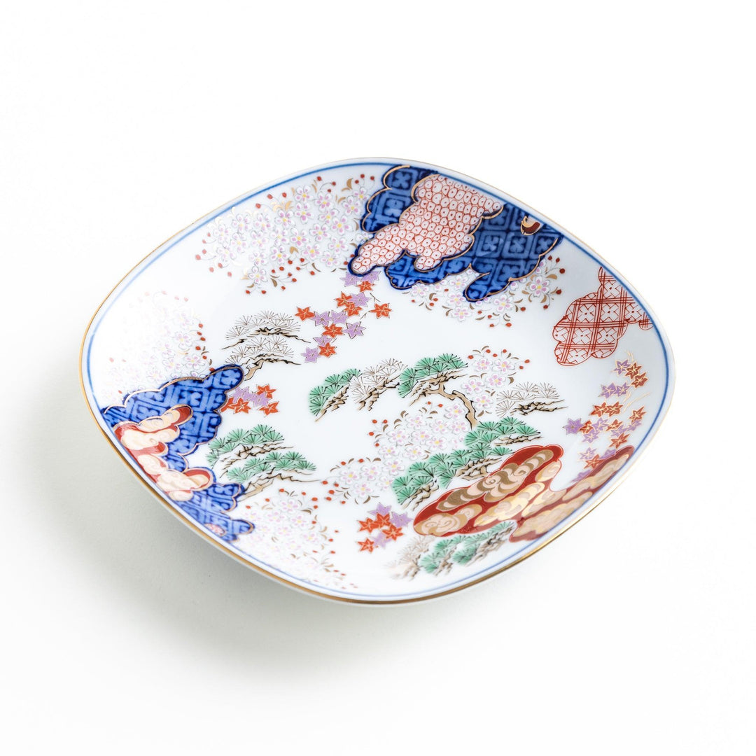 A square dessert plate featuring an intricate Japanese landscape with trees and clouds, surrounded by red and blue patterns on the border.