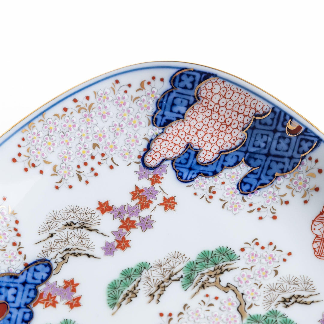 A square dessert plate featuring an intricate Japanese landscape with trees and clouds, surrounded by red and blue patterns on the border.