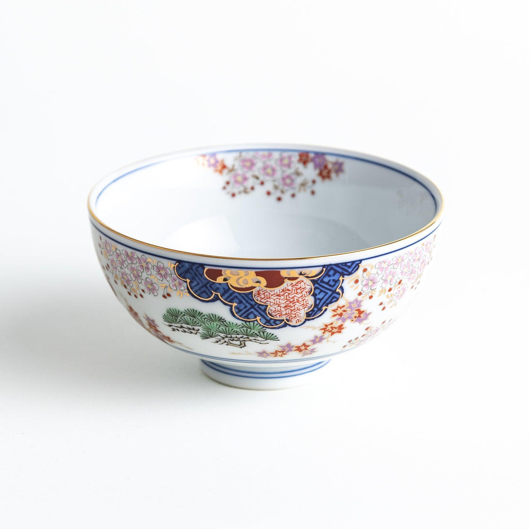 A round ceramic rice bowl with detailed traditional Japanese designs of trees and clouds in blue, red, and green on a white background.