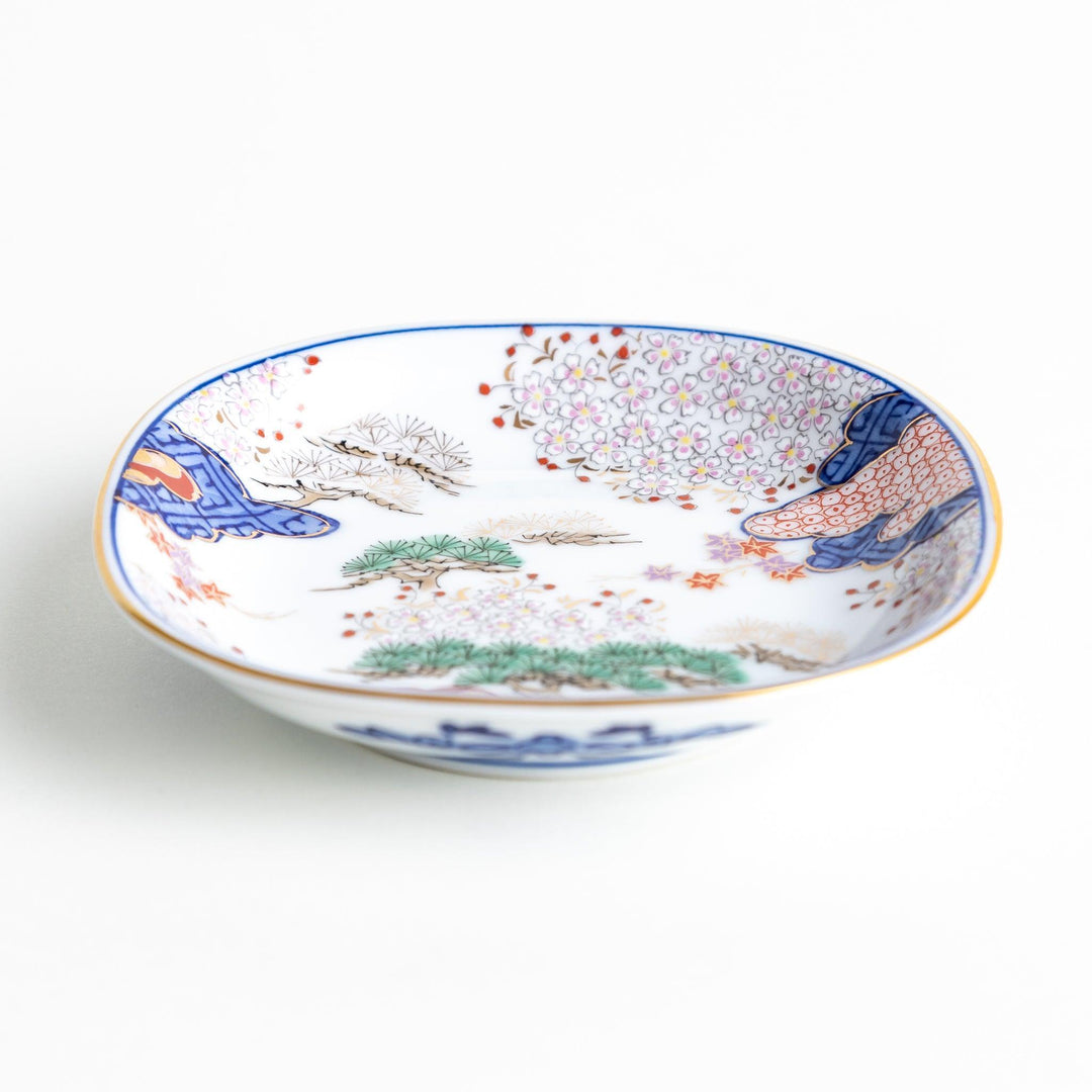 A square sauce dish featuring a traditional Japanese landscape with trees, clouds, and a golden sun, bordered by blue and red patterns.